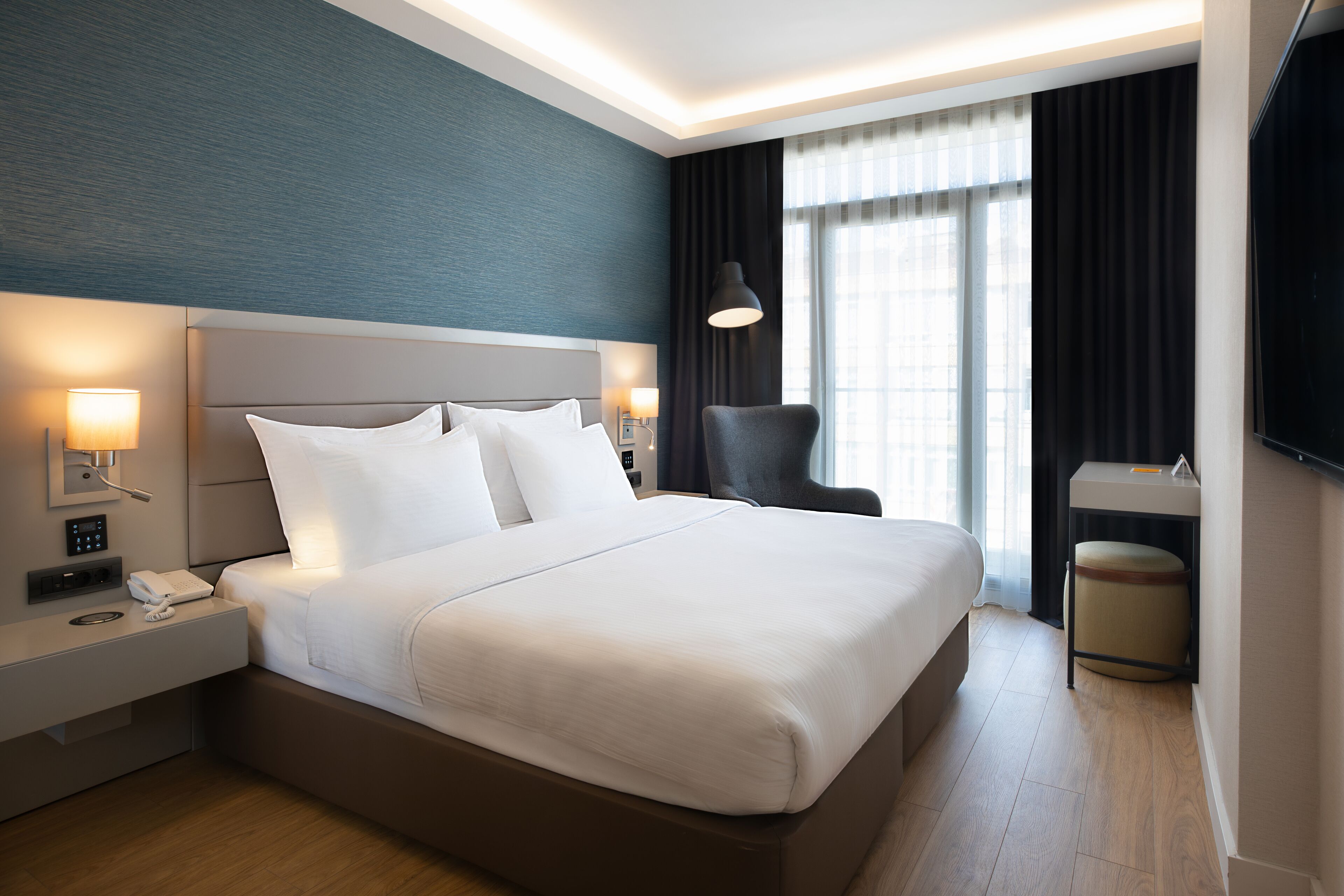 Una habitación de hotel moderna con una cama grande, lámparas de noche, un escritorio y un televisor.
