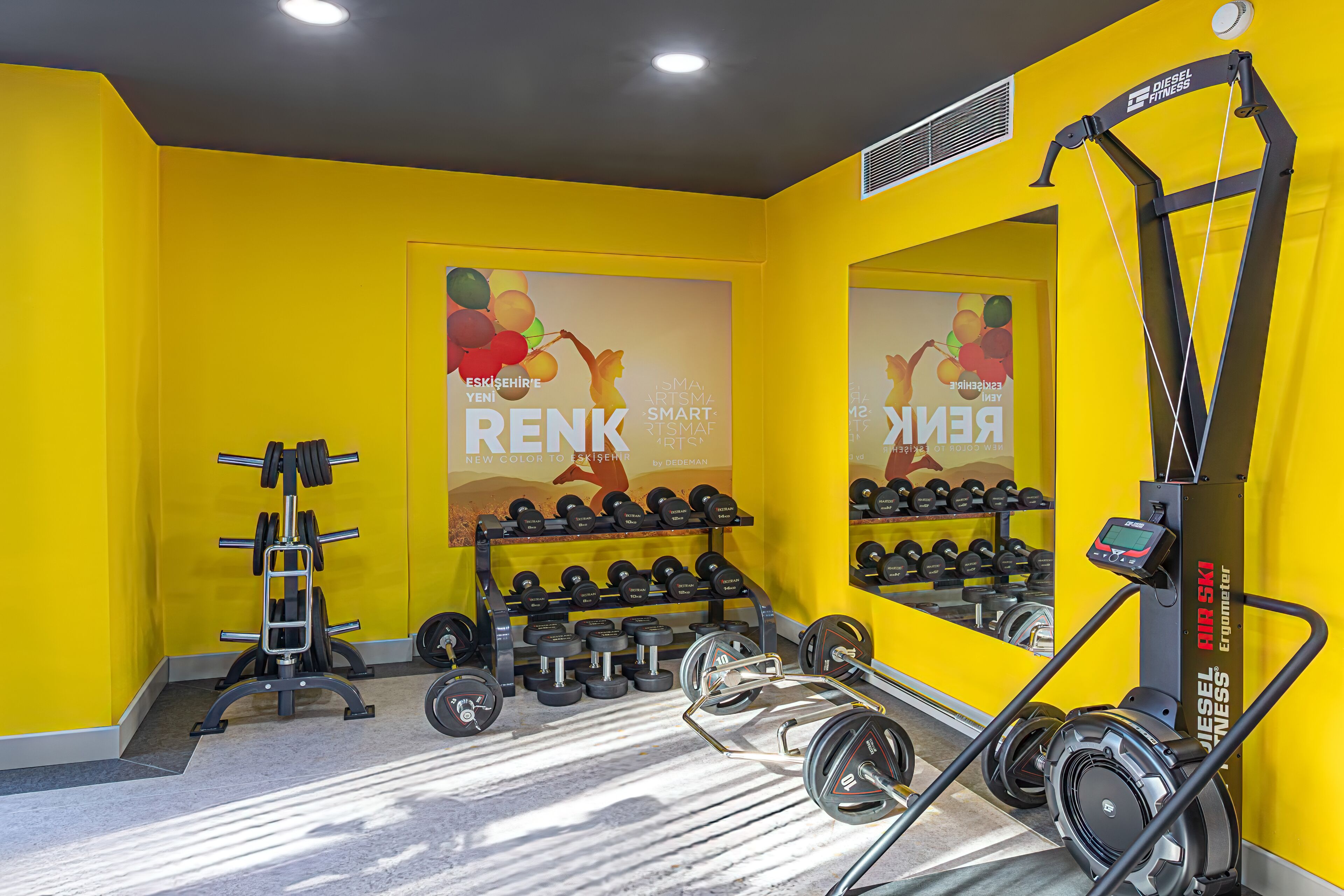 A gym with yellow walls, weightlifting equipment, and a mirrored wall.
