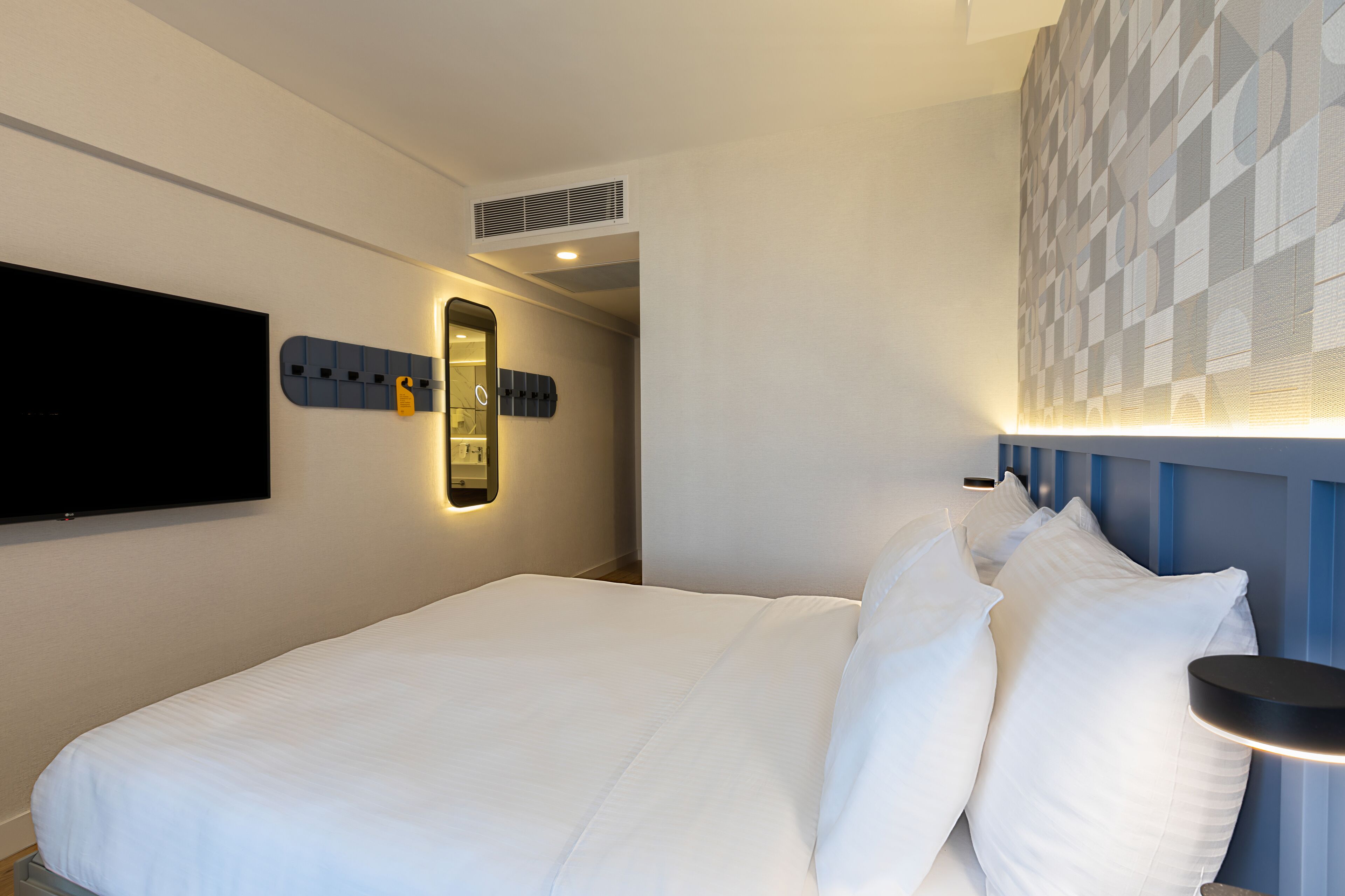 Une chambre d’hôtel dotée d’un grand lit, d’un téléviseur à écran plat fixé au mur, d’un miroir mural et d’un motif décoratif sur le mur.