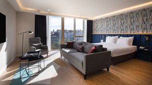 Une chambre d’hôtel moderne dotée d’un grand lit, d’un canapé, d’un bureau et offrant une vue sur la ville.