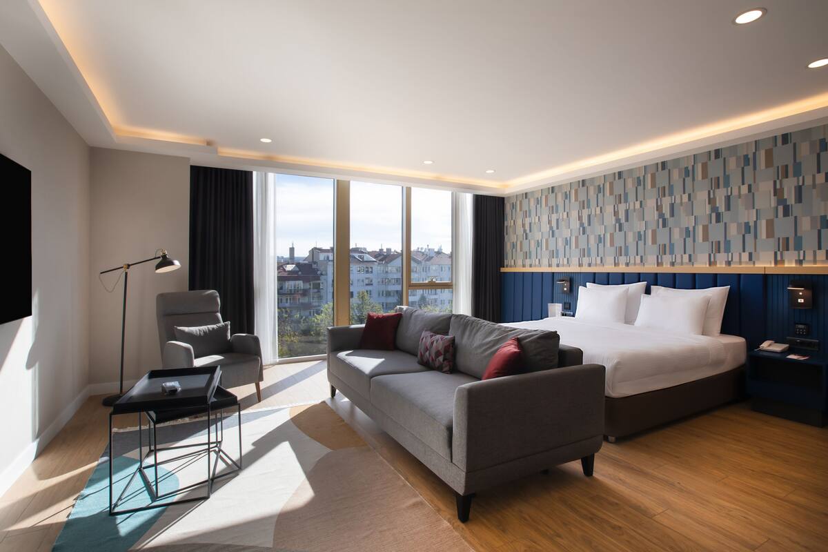 Een moderne hotelkamer met een groot bed, een zithoek, een bureau en uitzicht op de stad.