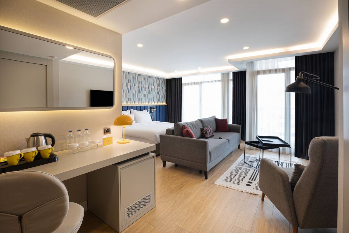 Een moderne hotelkamer met een bed, een bank, een bureau en een kleine kitchenette.