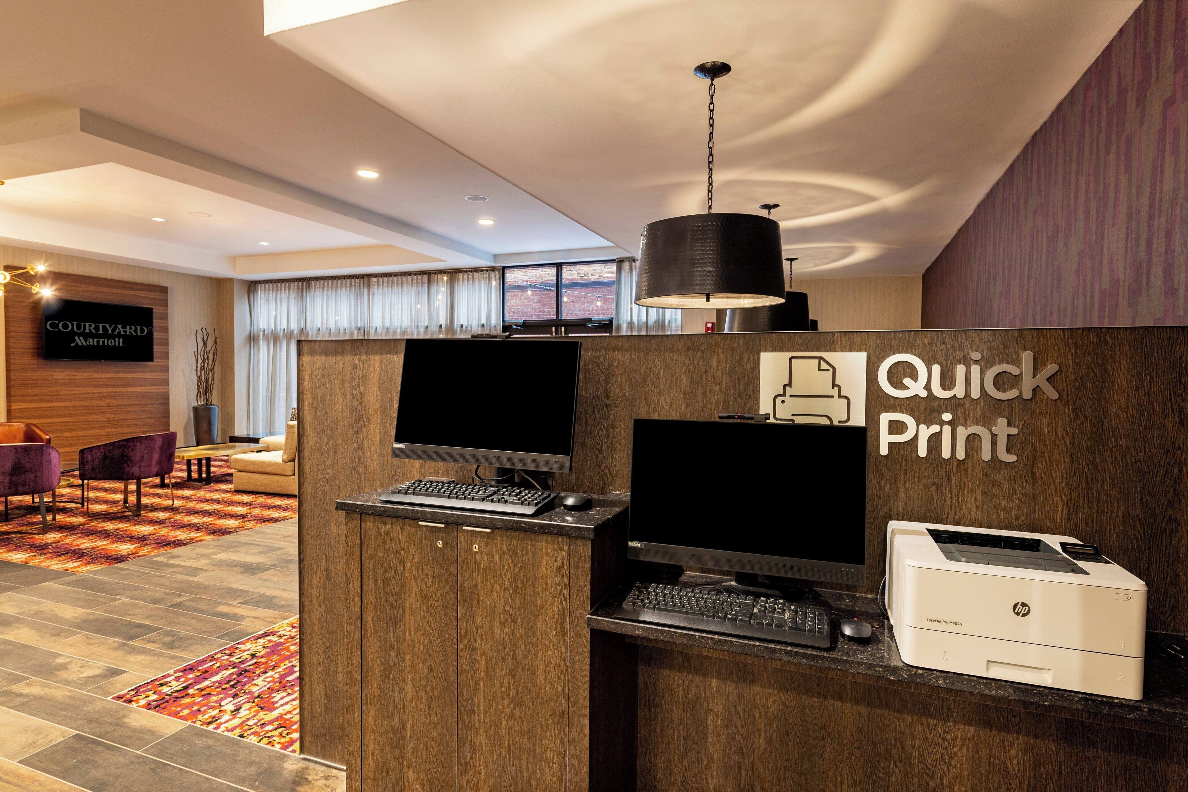 A hotel reception area with a 'Quick Print' service desk, a 'Courtyard Marriott' sign, and a view of the cityscape through the window.