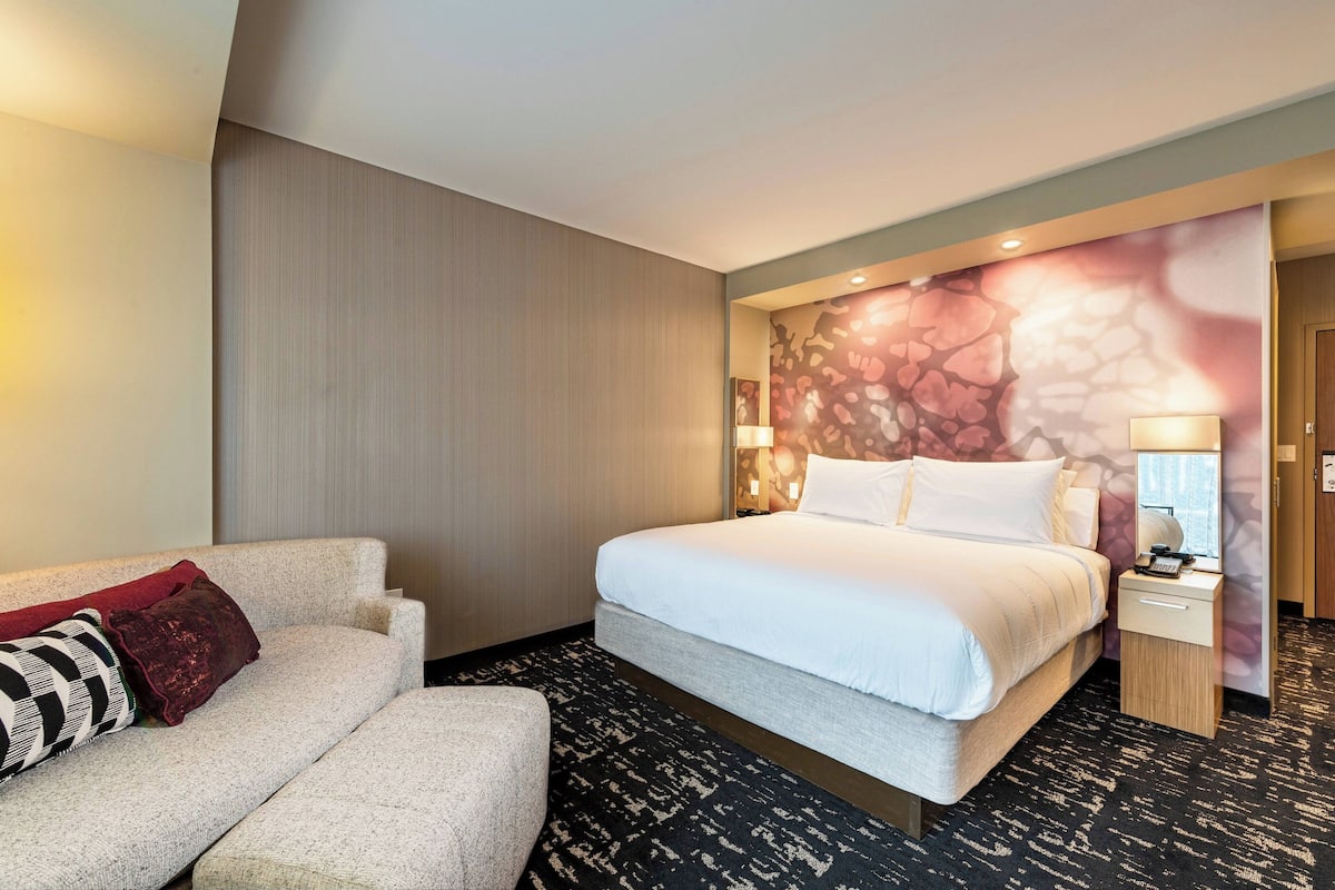 Une chambre d’hôtel comprenant un lit, un canapé, une table de chevet et un mur orné d’un motif floral.