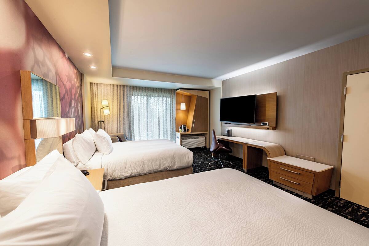 Une chambre d’hôtel avec deux lits, un bureau, une chaise, une télévision et une salle de bain avec douche et toilettes.