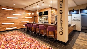 A modern bar area with wooden accents, bar stools, and a colorful rug. - Courtyard by Marriott Winston - Salem Downtown (Winston-Salem)
