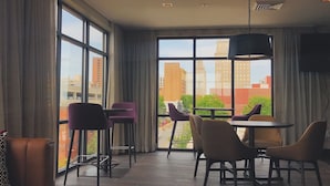 A modern hotel room with large windows, a dining area with chairs, a sofa, and a ceiling light fixture. - Courtyard by Marriott Winston - Salem Downtown (Winston-Salem)