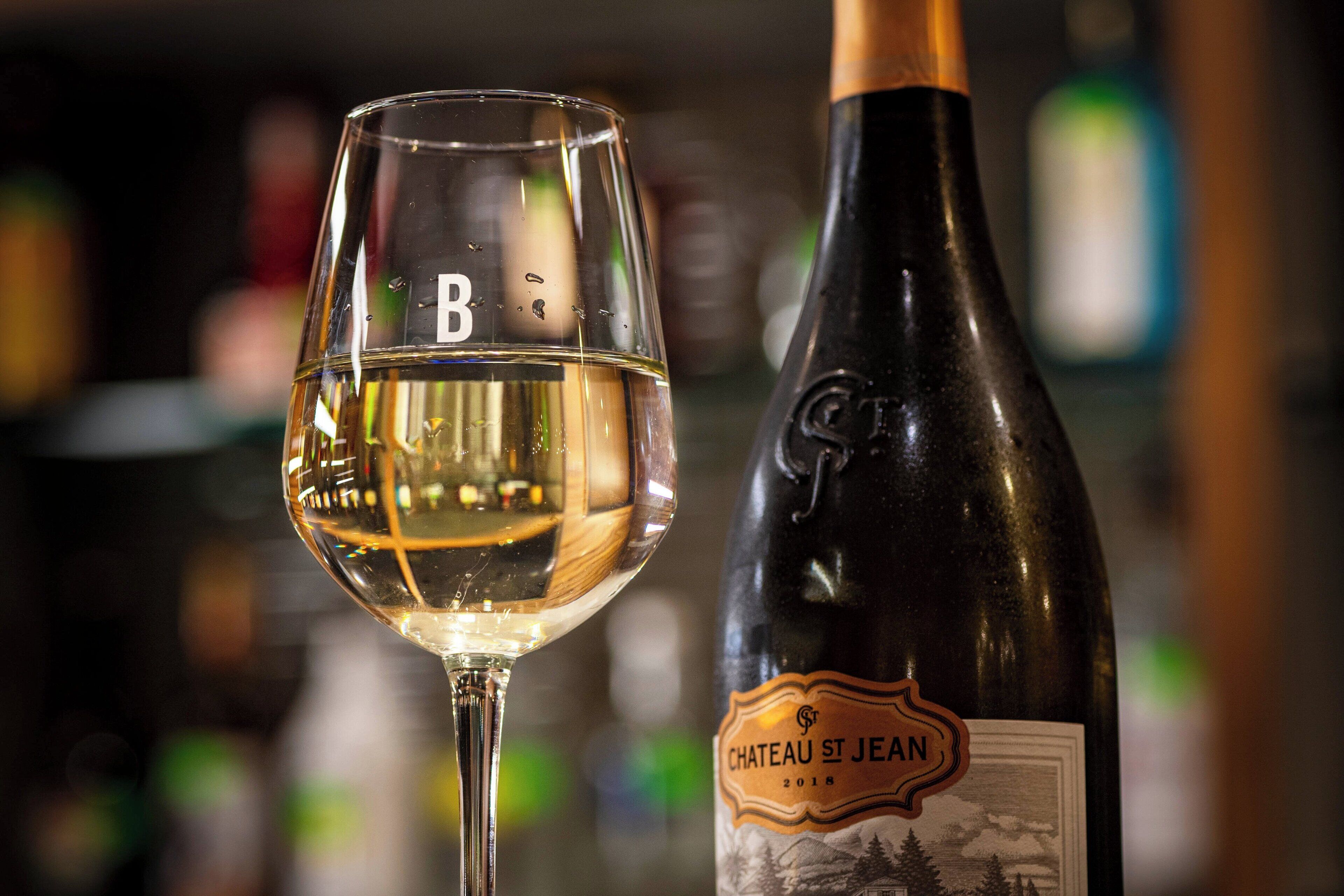 Una copa de vino con etiqueta y una botella de vino Chateau St Jean.