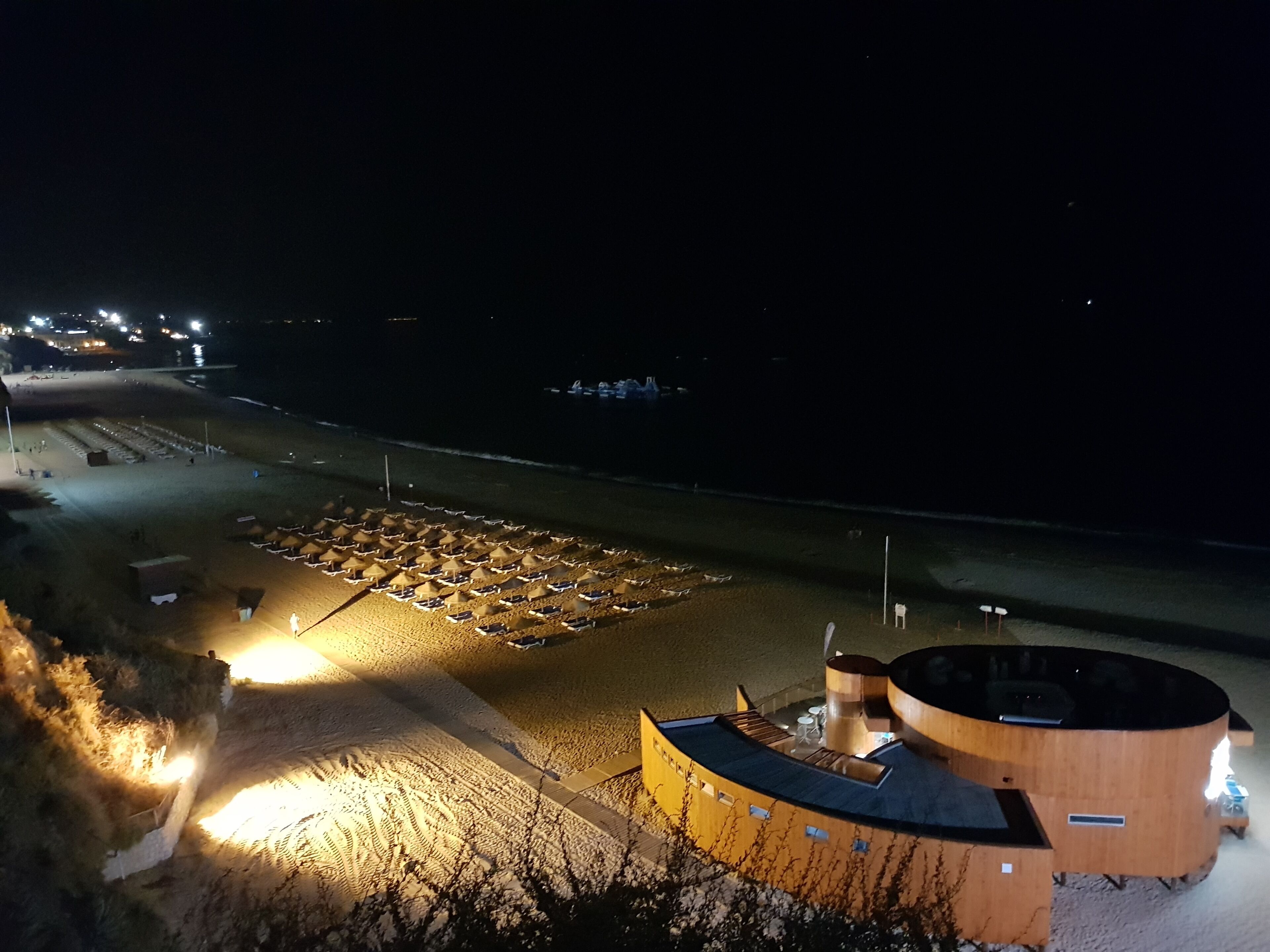 A beachside resort with a large sun umbrella area and a wooden building with a circular design.