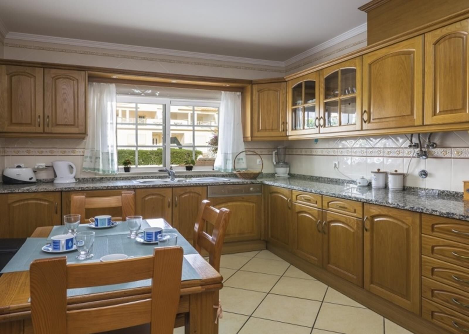 Een keuken met houten kastjes, een eettafel met stoelen, en een raam met gordijnen.