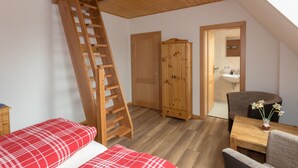 A bedroom with a wooden ladder, a wardrobe, a desk with a vase of flowers, and a view of a bathroom through an open door. - Haus Lutki (Burg (Spreewald))