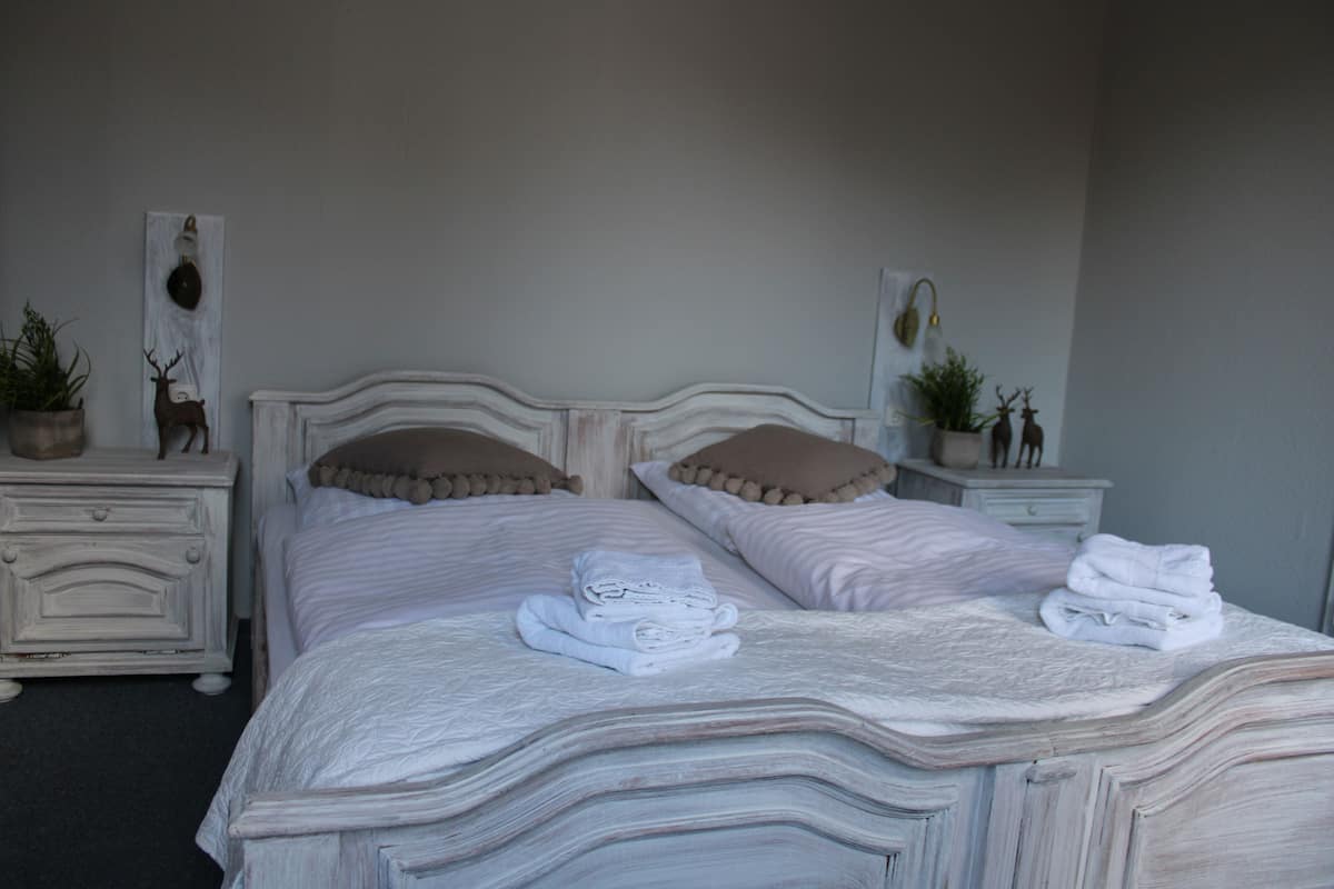 A neatly made bed with folded towels, a headboard, and two bedside tables with decorative items.
