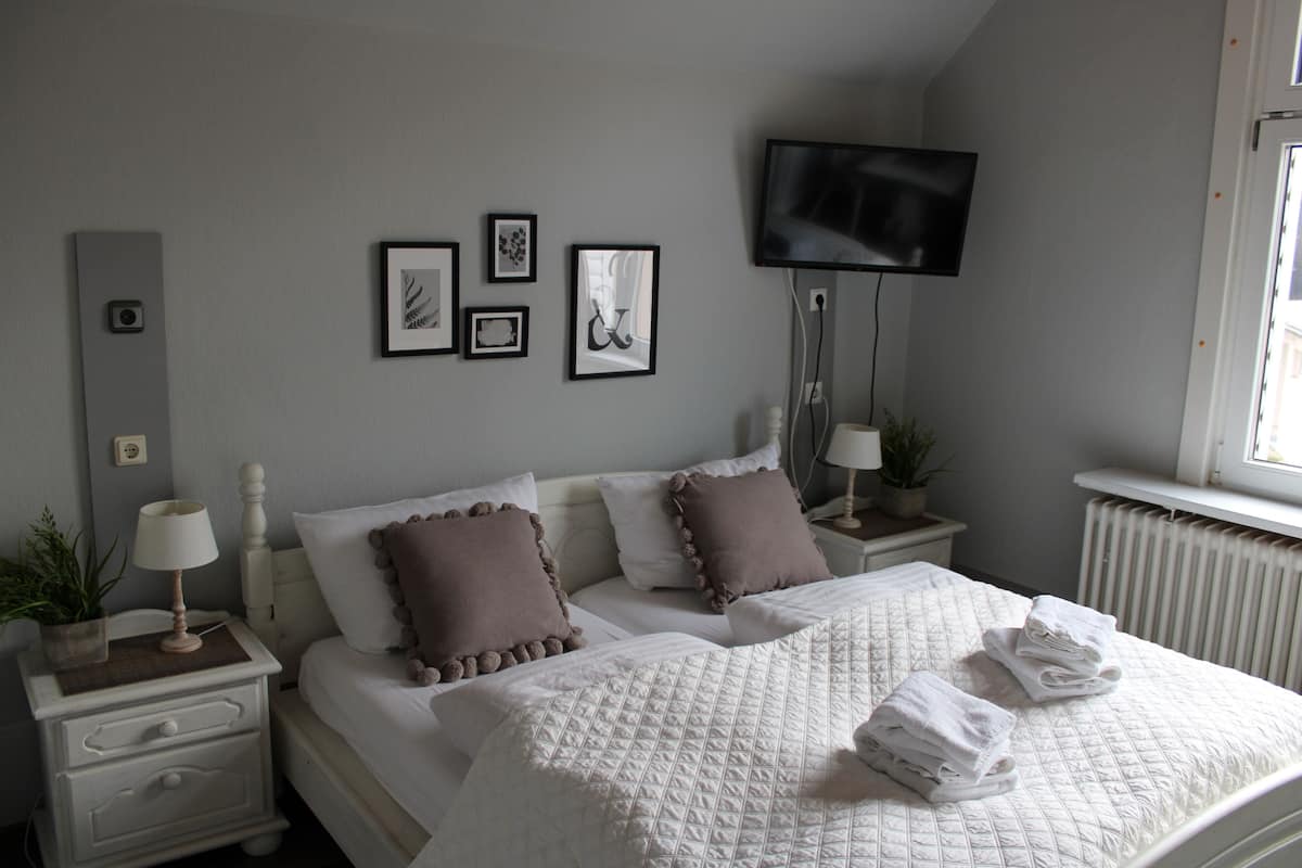 A bedroom with a bed, two bedside tables, a TV, and framed pictures on the wall.