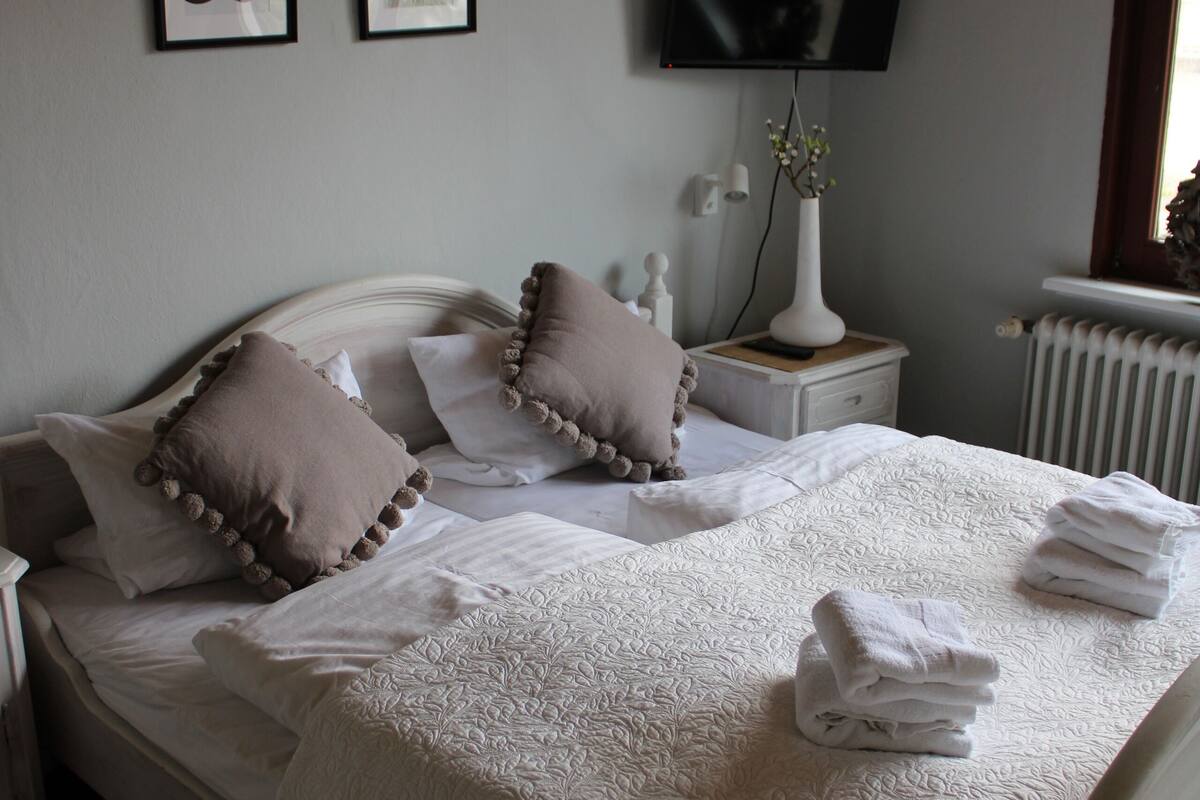 A neatly made bed with a white bedspread and pillows, a bedside table with a lamp, and two framed pictures on the wall.