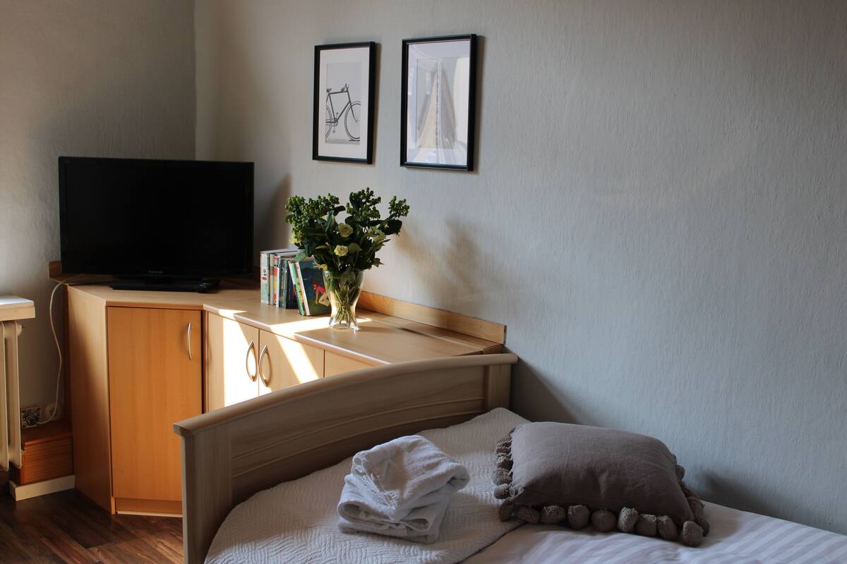 A neatly arranged hotel room with a bed, a TV, a bedside table with a vase of flowers, and two framed pictures on the wall.
