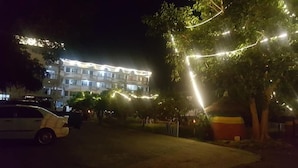 Un immeuble à étages, un espace de stationnement et un arbre décoré de guirlandes lumineuses.