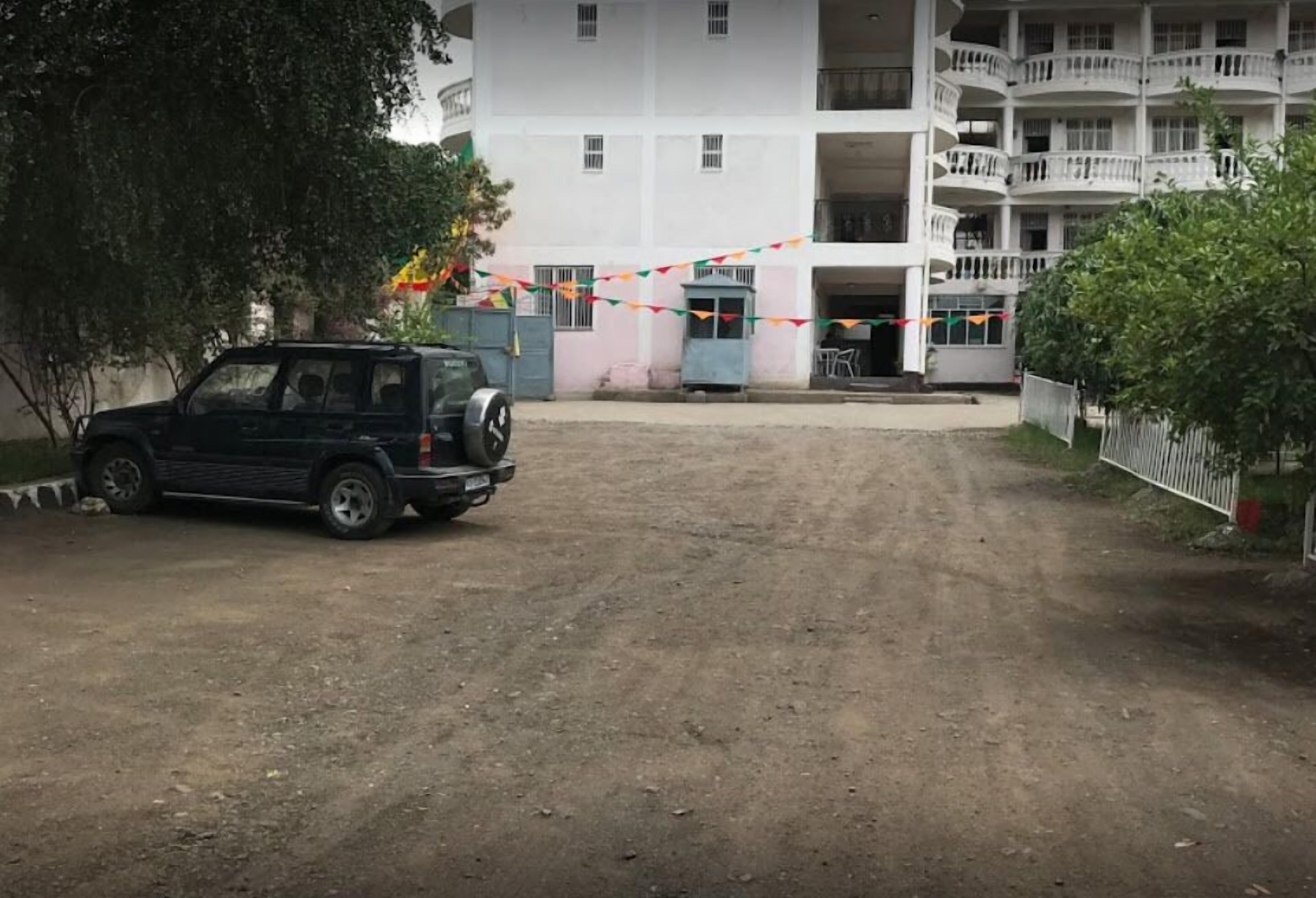 A dirt road leading to a multi-story building with balconies.