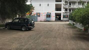 A dirt road leading to a multi-story building with balconies.