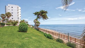 Un hotel frente al mar con césped, palmeras y vistas a la playa.