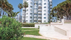 Un edificio de varios pisos con balcones, rodeado de follaje y palmeras.