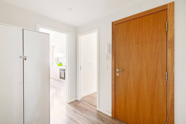 A hallway with a wooden door, a white door, and a view into a kitchen area.