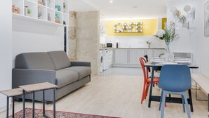 A modern living room with a grey sofa, a dining table with chairs, and a kitchen area with a 'CAFE' sign. - Hedonist House - Design Loft Design in  Heart of Paris ! (Paris)