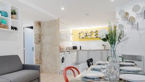 A modern living room with a grey sofa, a dining table set with plates and glasses, and a kitchen in the background with a 'CAFE' sign. - Hedonist House - Design Loft Design in  Heart of Paris ! (Paris)