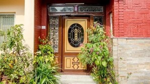 Une entrée d’immeuble avec une porte en bois, des plantes en pot et un chemin dallé menant à la porte.