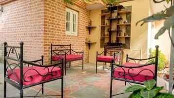 Un patio con paredes de ladrillo, sillas de metal con cojines rojos y un estante contra la pared.