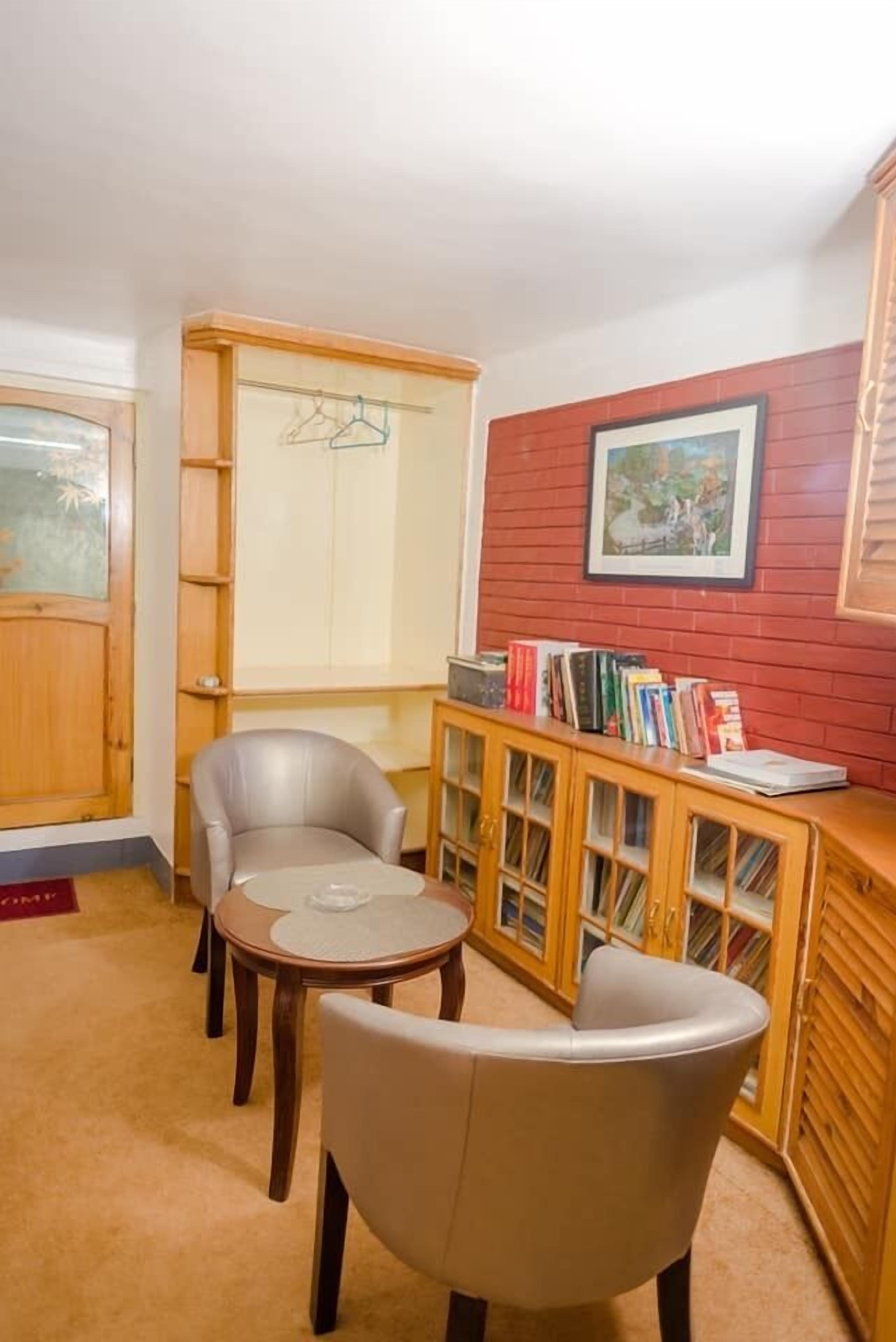 Una habitación con un armario de madera, dos sillas, una mesita y una estantería llena de libros.