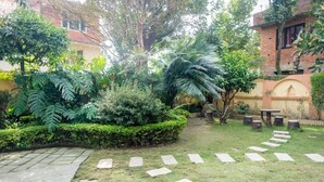 Un jardin avec un chemin de pierres, une végétation luxuriante et un petit espace aménagé avec une table et des chaises.