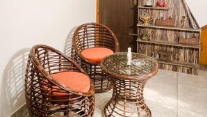 Une pièce avec des chaises en osier et une table en verre, un escalier en bois doté d’étagères et un tableau encadré au mur.