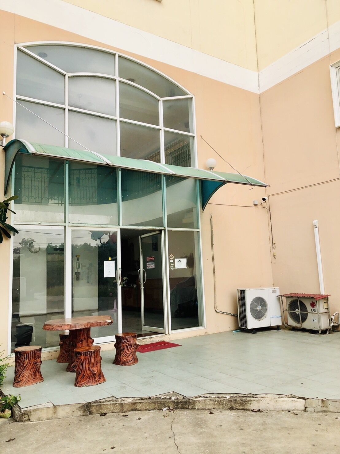 A building with a glass entrance, outdoor seating with wooden stools, and an air conditioning unit.