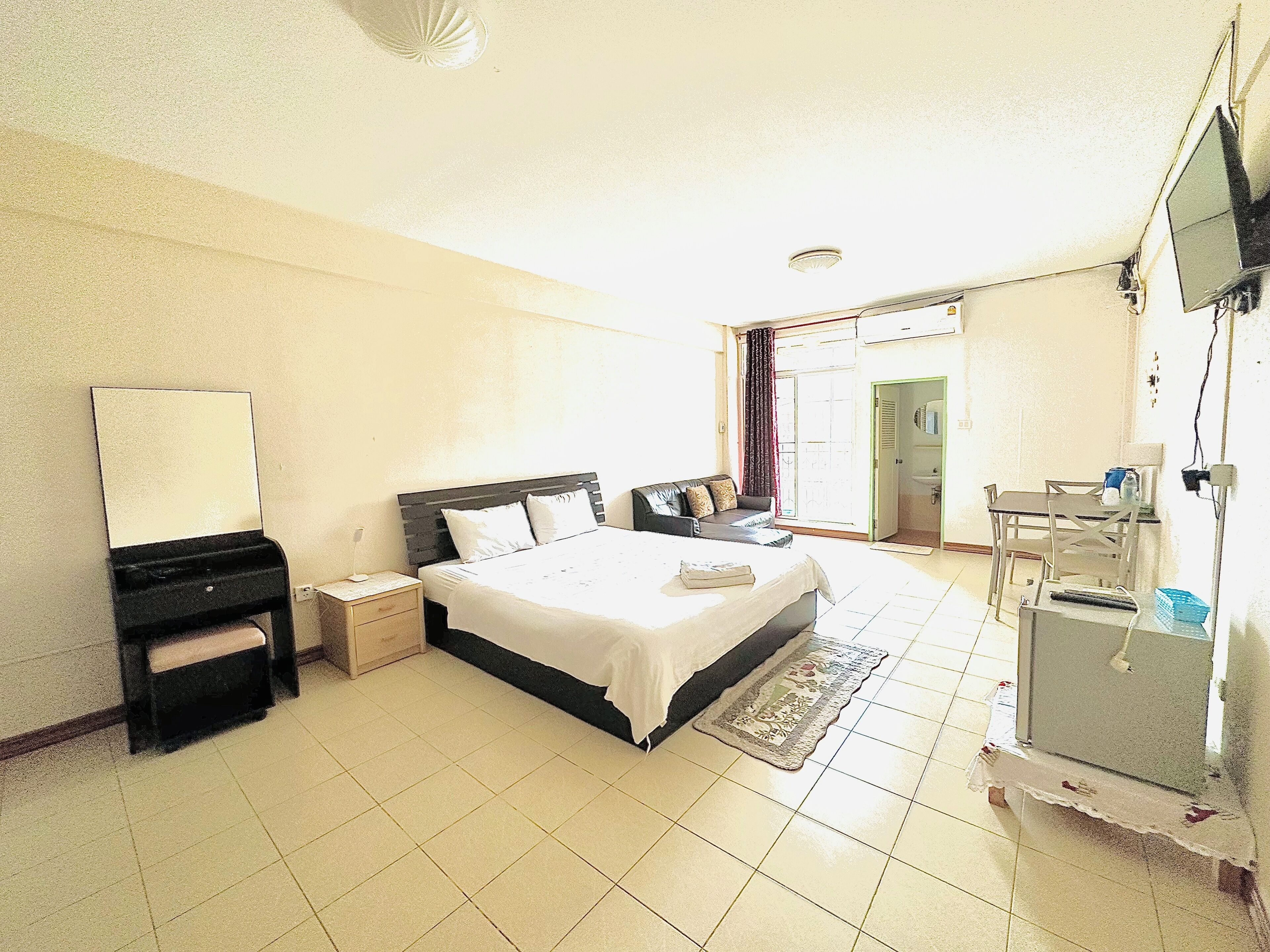 A hotel room with a bed, bedside table, dresser, mirror, and a desk with a chair.