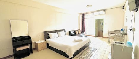 A hotel room with a bed, bedside table, dresser, mirror, and a desk with a chair.