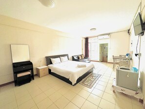 A hotel room with a bed, bedside table, dresser, mirror, and a desk with a chair. - VK & Residence Kanchanaburi (Kanchanaburi)