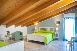 A bedroom with a sloped ceiling, a bed with a green bedspread, a green armchair, a small table with a lamp, and a window with blue curtains. - B&B La Canfora (Atri)