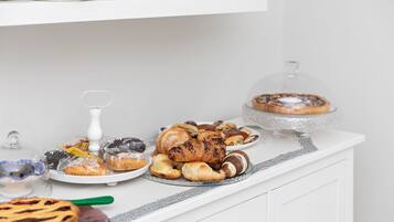 Un tavolo per buffet con diversi dolci e pasticcini, tra cui una torta coperta e una ciotola di vetro con un cucchiaio verde.