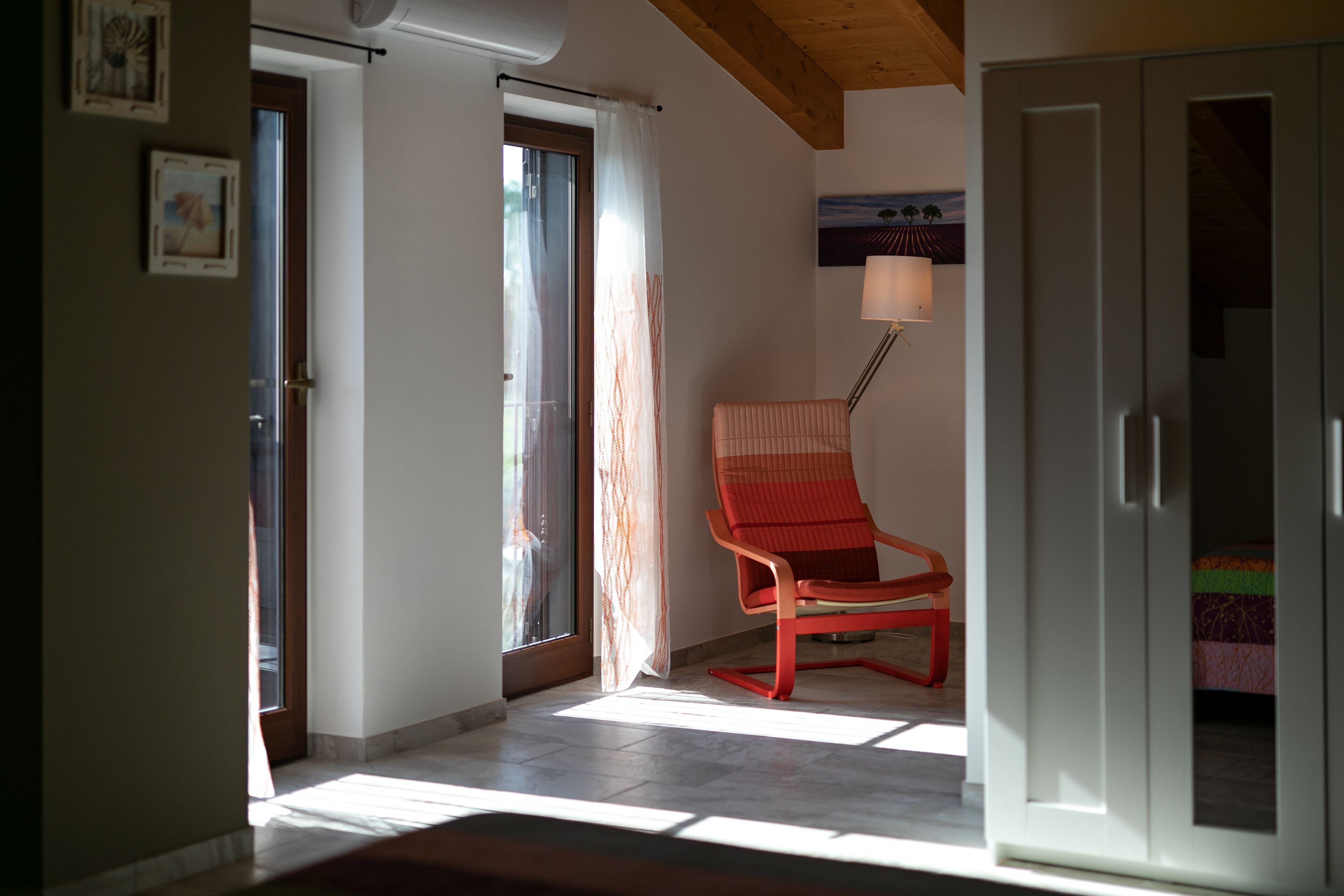 A room with a red chair, a bed, a wardrobe, and a painting on the wall.