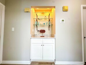 A hallway with a white door, a glass shelf with decorative items, and a light fixture above it. - Tilghman Beach and Racquet Club 320 (North Myrtle Beach)