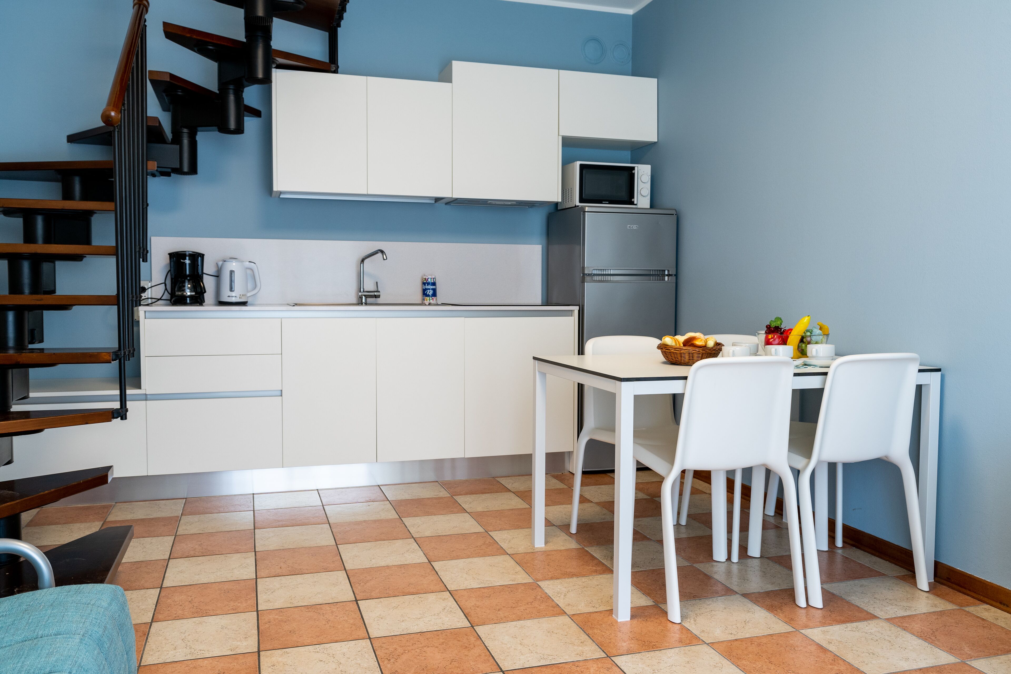 Una cocina moderna con armarios blancos, microondas, refrigerador, cafetera y una mesa de comedor con sillas.