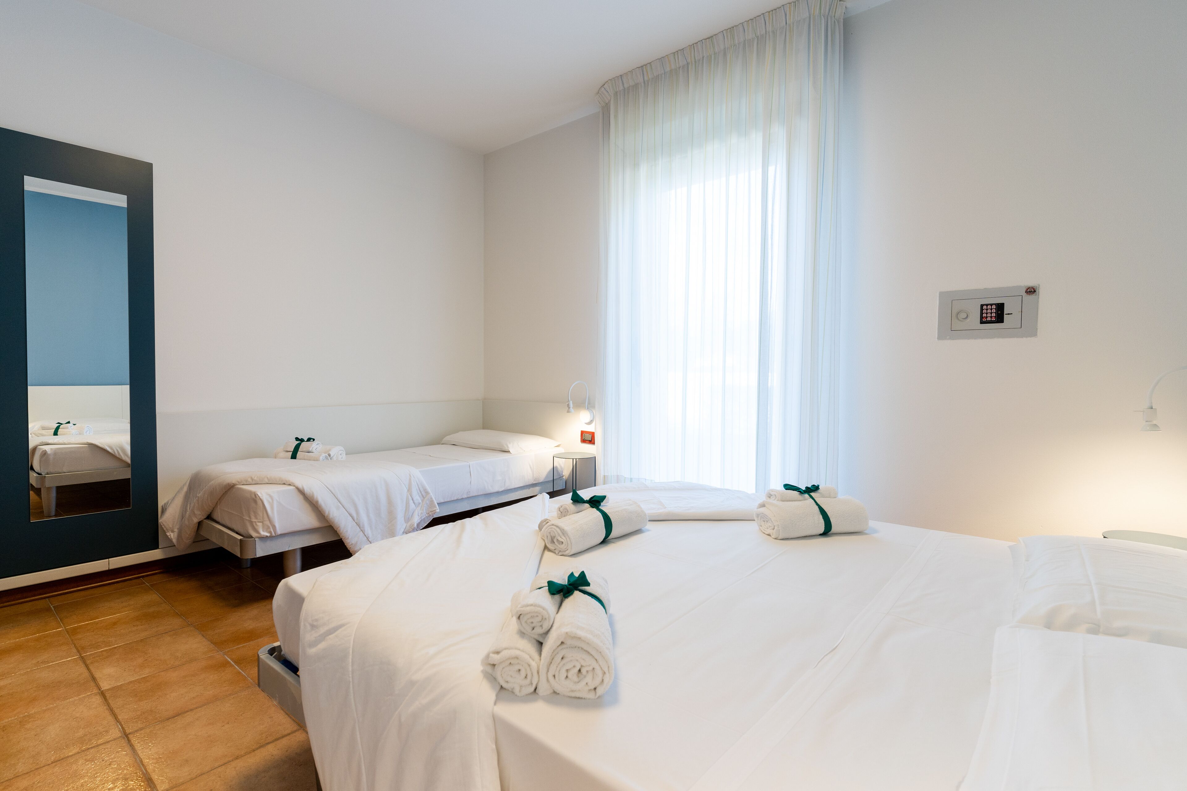 Een hotelkamer met twee bedden, een badkamer en een groot raam met gordijnen.