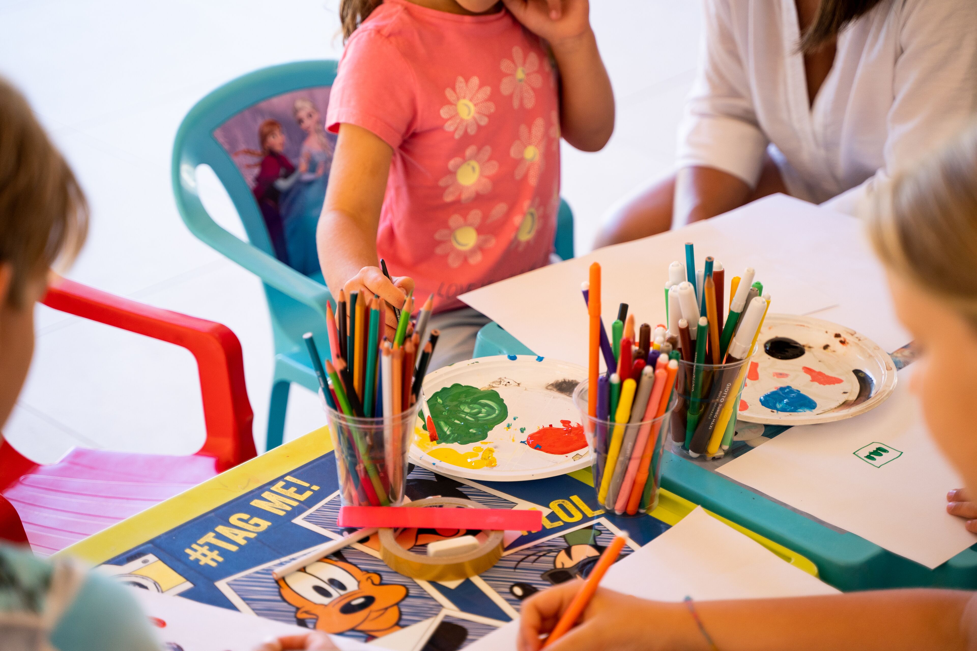 Un grupo de niños participan en una actividad de pintura con diversos materiales artísticos sobre una mesa.