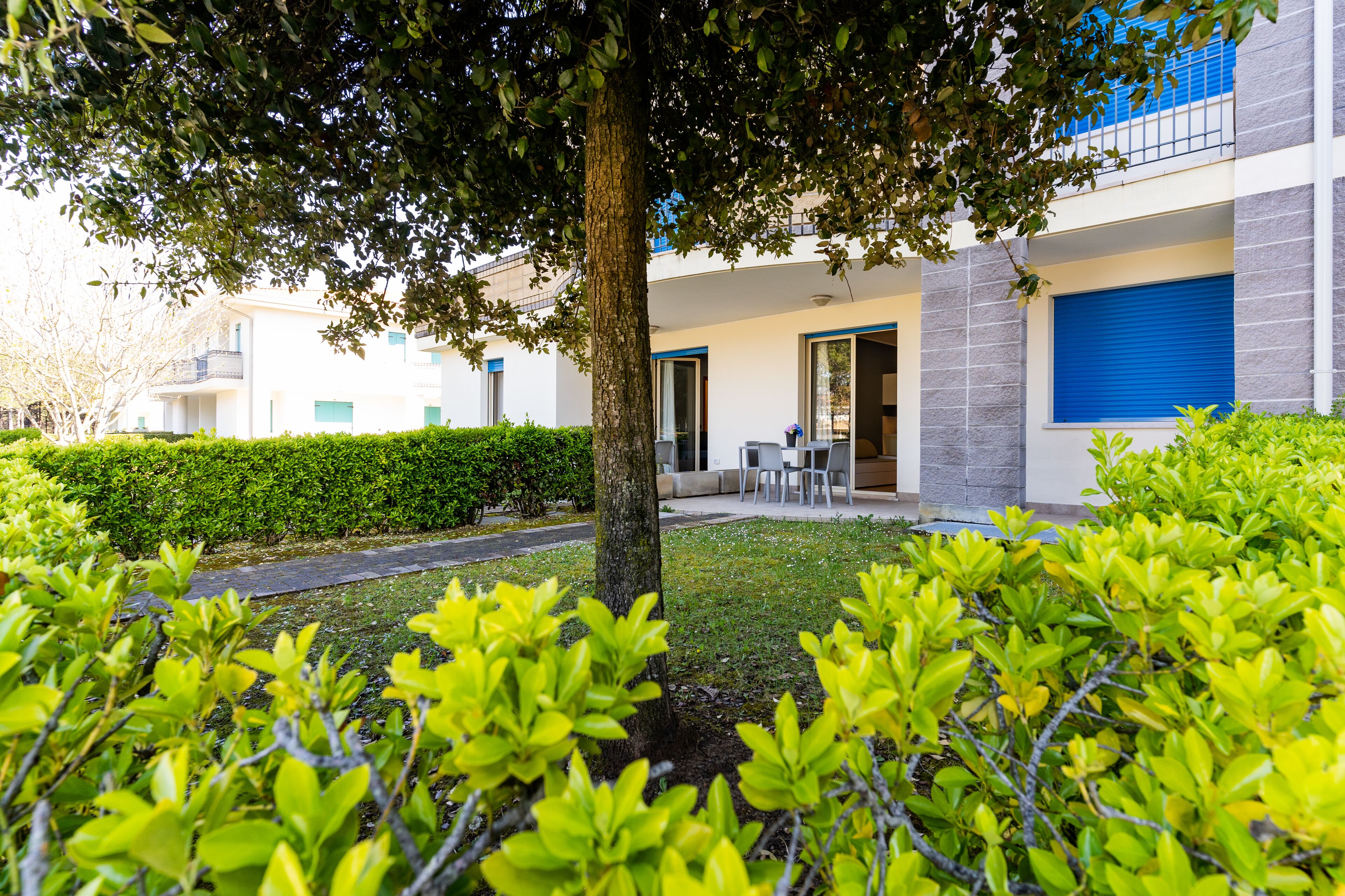 A modern building with a covered outdoor seating area, surrounded by well-maintained greenery.