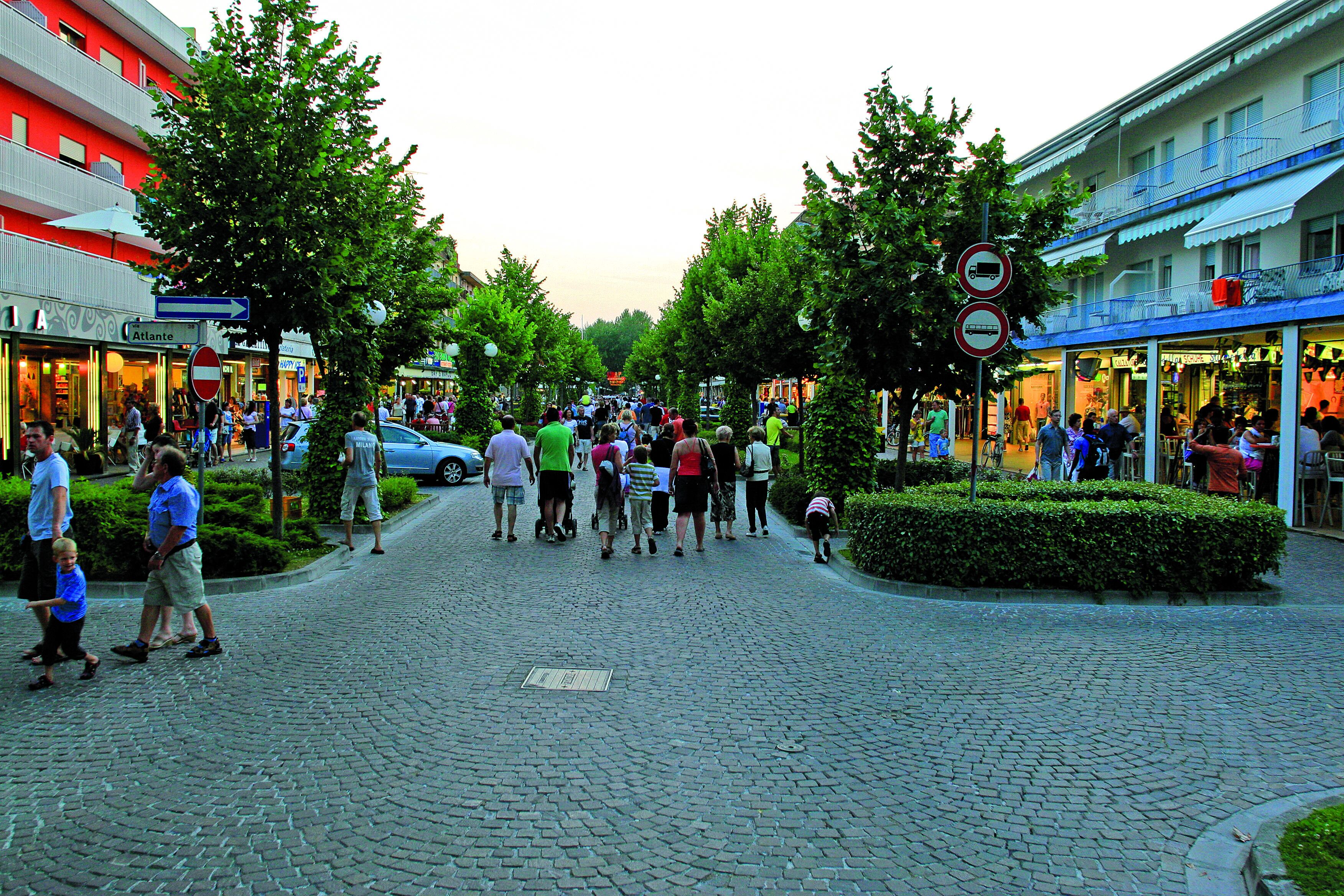 A cobblestone street lined with trees and buildings, including a hotel with balconies and outdoor seating.