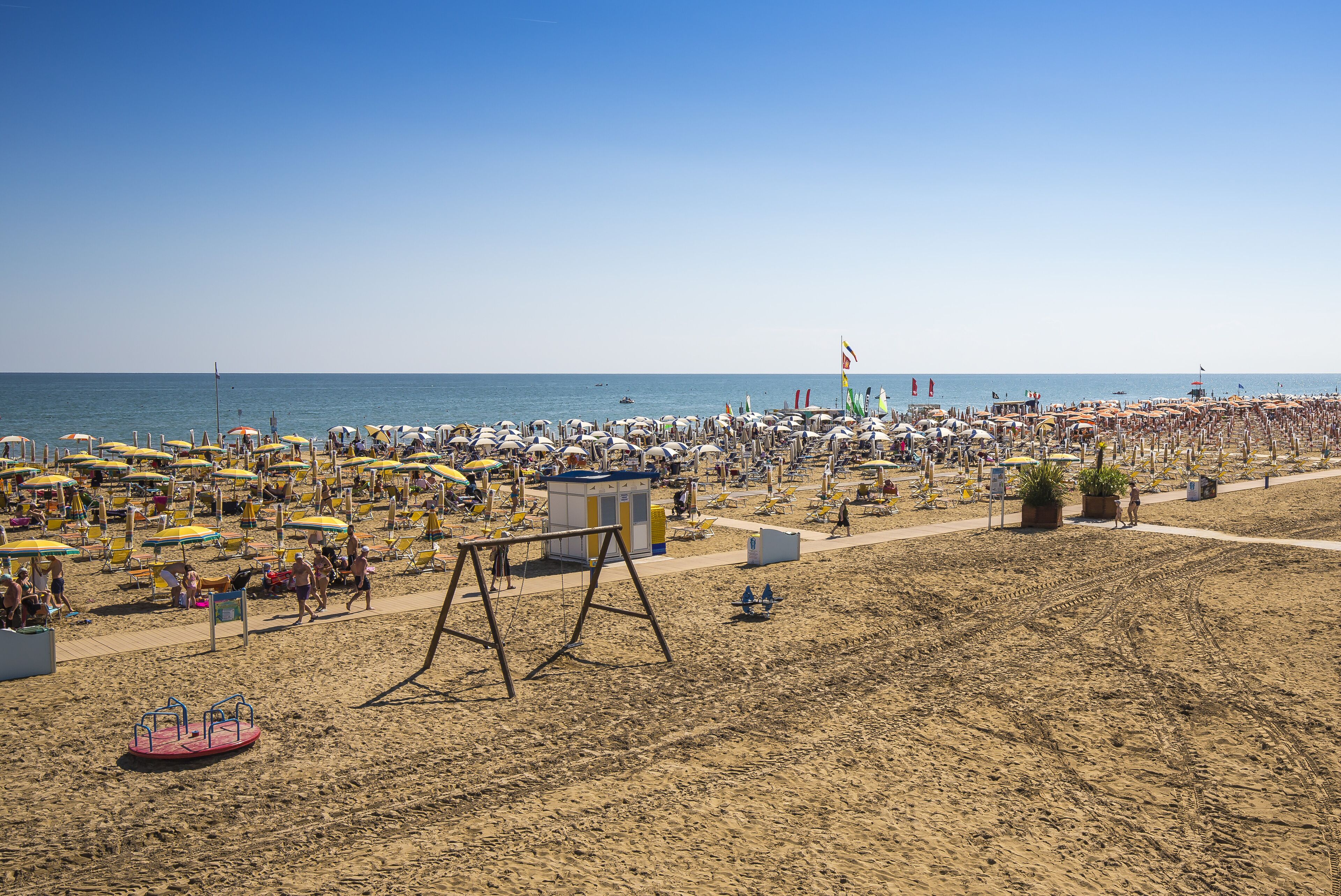 Una spiaggia con numerosi ombrelloni e lettini, una torretta per i bagnini e una passerella sabbiosa.