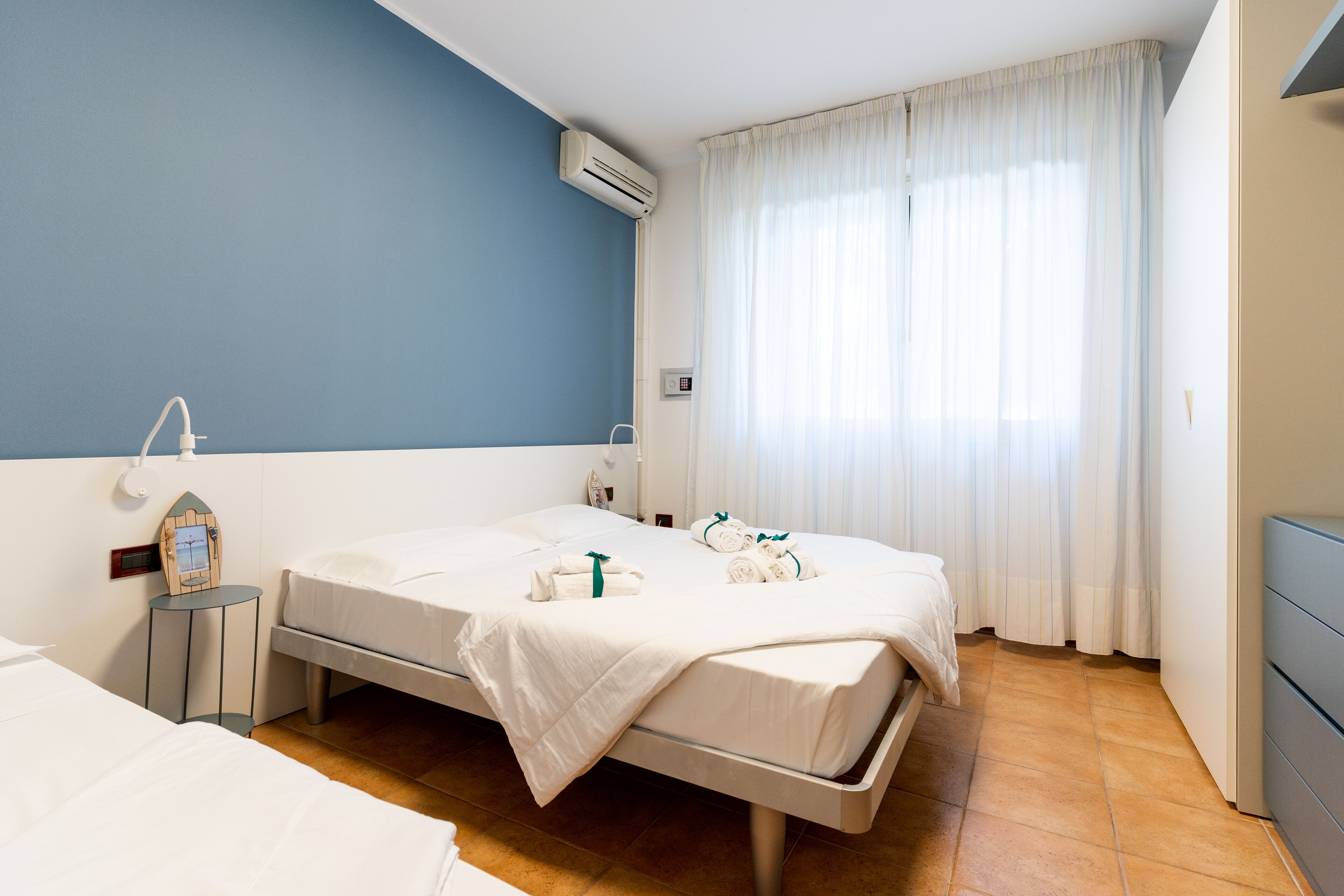 Une chambre d’hôtel avec deux lits, une horloge au mur et une fenêtre avec des rideaux.