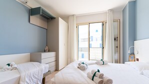 Ein Hotelzimmer mit zwei Betten, einem Nachttisch, einem Kleiderschrank und Blick nach draußen.