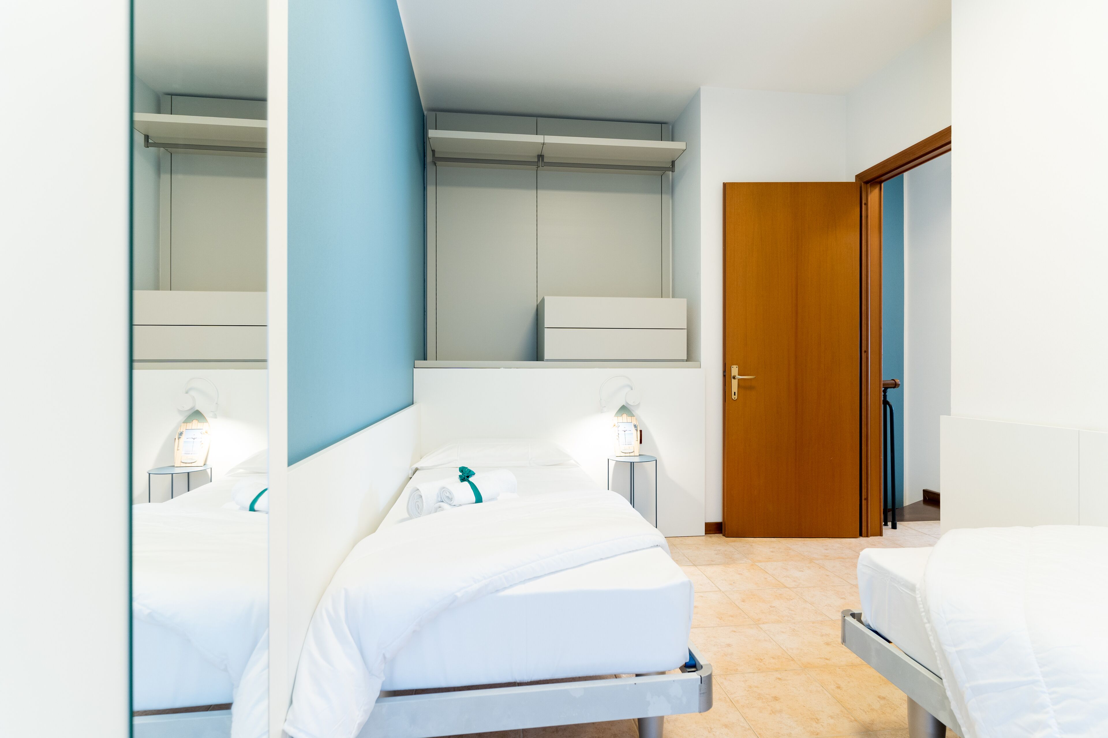Une chambre d’hôtel avec deux lits, une armoire, une table de chevet avec une lampe et une porte donnant sur une autre pièce.