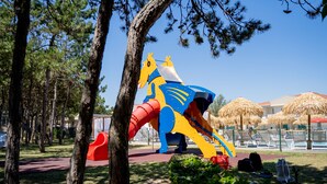 Ein Spielplatz mit einer großen Hüpfburg und Klettergerüsten, umgeben von Bäumen und blauem Himmel.